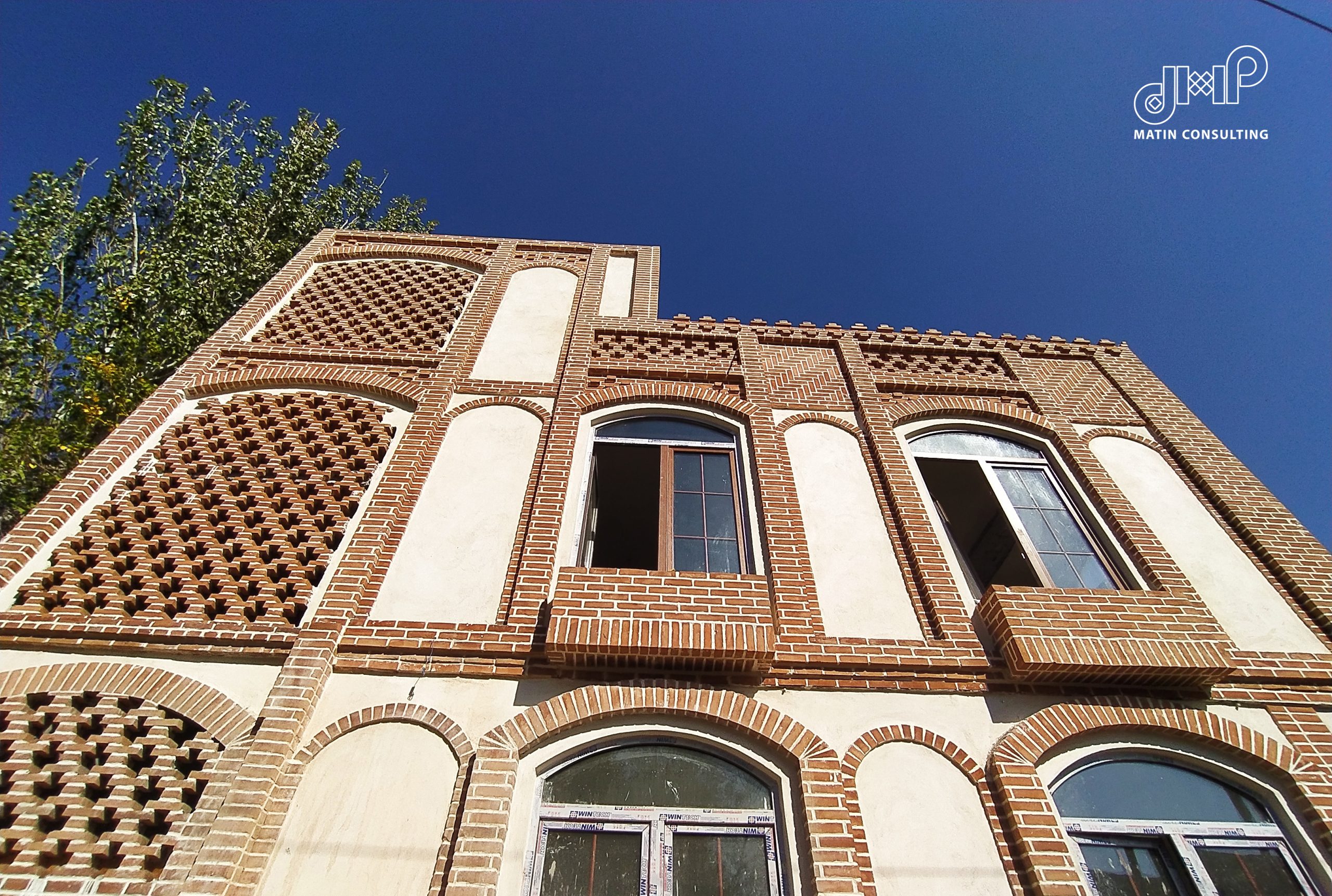 ردیف قاب‌های قوسی مشبک و جان‌پناه آجری در نمای عمارت ربیعی